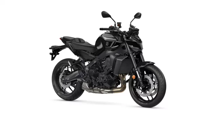 Black sport motorcycle photographed from the left side, showing engine, exhaust, and large disc brakes at the front and rear is visible beneath the frame.