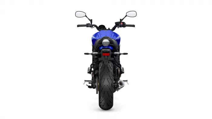 Rear view of a blue sport motorcycle showing a wide rear tire, round tail light, and prominent exhaust beneath the seat from the back perspective with side mirrors visible