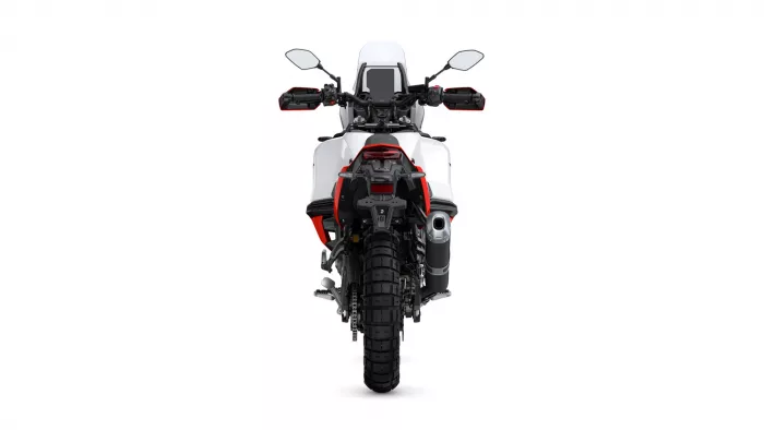 Rear view of a white adventure motorcycle with red accents, large knobby rear tire, and visible exhaust on the right side against a white background.