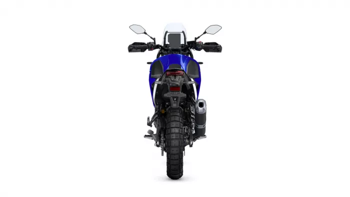 Rear view of a blue dual-sport motorcycle showing a large off-road rear tire, taillight, and exhaust on the right side.