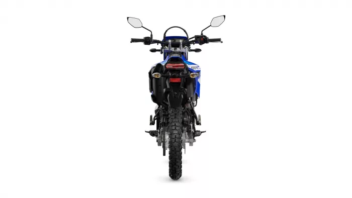 Rear view of a blue off-road motorcycle, showing the red taillight, mirrors, and a knobby rear tire.