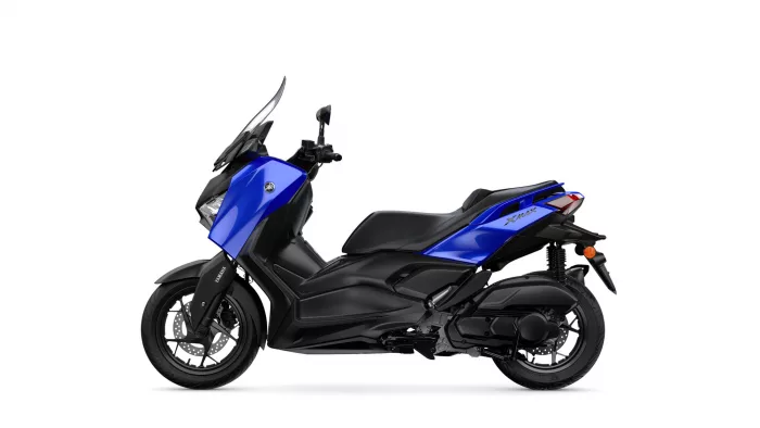 Blue Yamaha XMAX scooter viewed from the left side, showing its blue body panels, black chassis, windshield, and front wheel with disc brake exit.