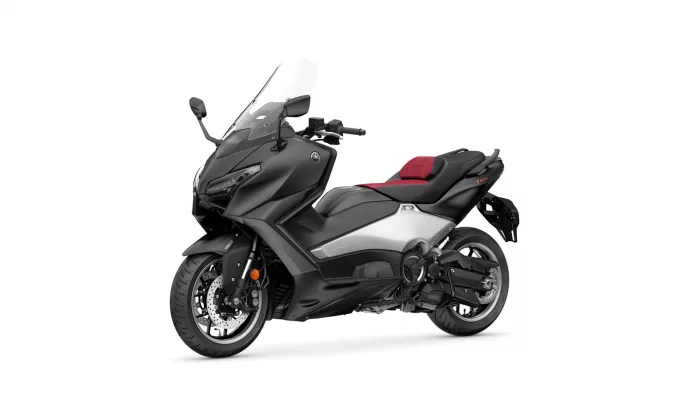Black and gray Yamaha Tmax motorcycle scooter with a red seat, angled to the left, showing its windshield and front headlight.