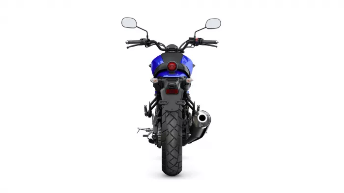 Rear view of a blue motorcycle showing chunky rear tire, single round red taillight, and dual side mirrors from the rider position