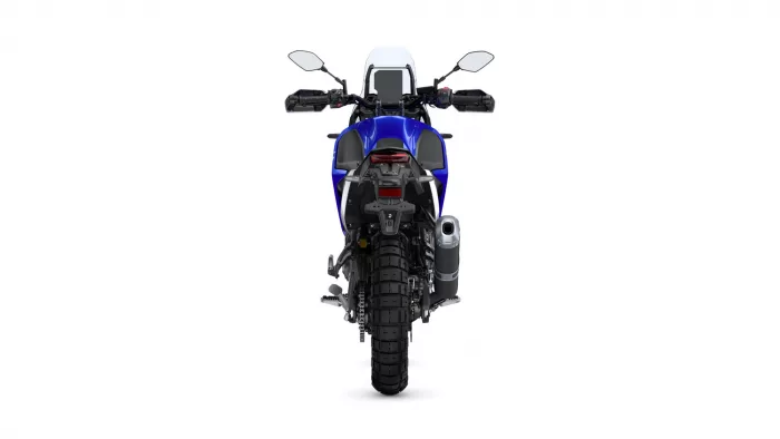 Rear view of a blue adventure motorcycle showing taillight, wide rear tire, and exhaust on the right side.