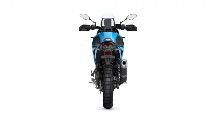 Rear view of a blue adventure motorcycle, showing the taillight, wide rear tire, exhaust on the right, and handlebars with mirrors.