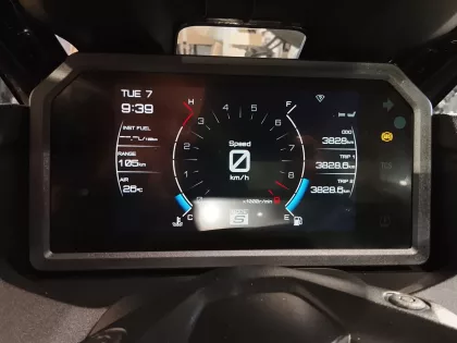 Digital car instrument cluster showing speed at 0 km/h, odometer 3,828 km, and trip data; fuel range 105 km, outside temperature 26°C, time Tue 9:39, date Tue 7; warning lights (ABS) visible on right.