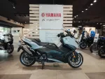 Blue Yamaha scooter on display in a showroom with other motorcycles and a Yamaha sign in the background.