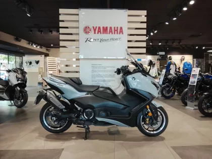 Blue Yamaha scooter on display in a showroom with other motorcycles and a Yamaha sign in the background.