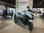 Showroom scene with a light blue Yamaha sport bike in the foreground and other motorcycles in the background beneath a Yamaha sign, showroom displays visible behind them.