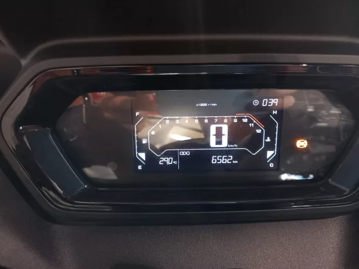 Digital car instrument cluster showing speed at 0 km/h, tachometer up to 12, fuel gauge on left, engine temp on right, odometer 65662 km, and external temp 29.0°C with a warning light on.