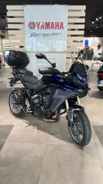 Blue Yamaha sport-t touring motorcycle on a showroom floor with a large Yamaha banner in the background and a top case mounted behind the seat.