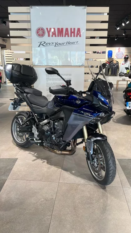 Blue Yamaha sport-t touring motorcycle on a showroom floor with a large Yamaha banner in the background and a top case mounted behind the seat.