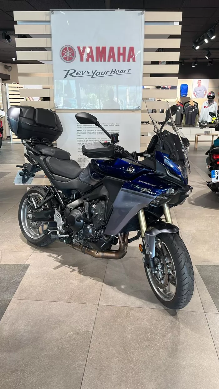 Blue Yamaha sport-t touring motorcycle on a showroom floor with a large Yamaha banner in the background and a top case mounted behind the seat.