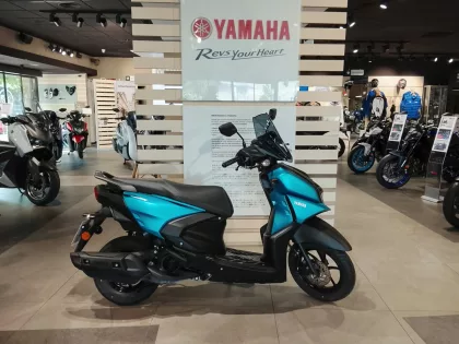 Blue Yamaha scooter in the foreground inside a Yamaha showroom with other motorcycles on display in the background