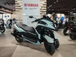 Mint-green Yamaha scooter on display inside a showroom with other bikes and a Yamaha sign above.