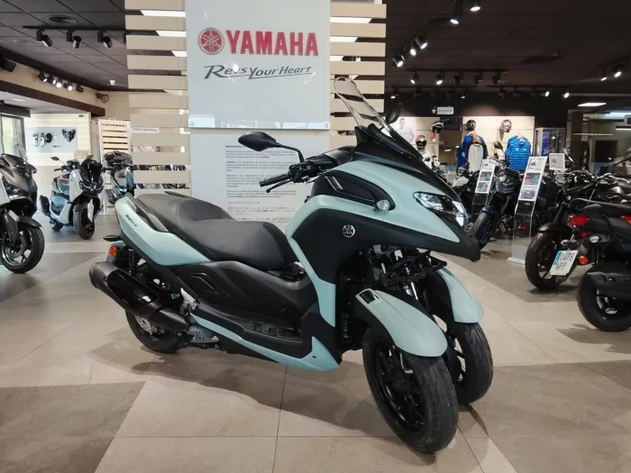 Mint-green Yamaha scooter on display inside a showroom with other bikes and a Yamaha sign above.